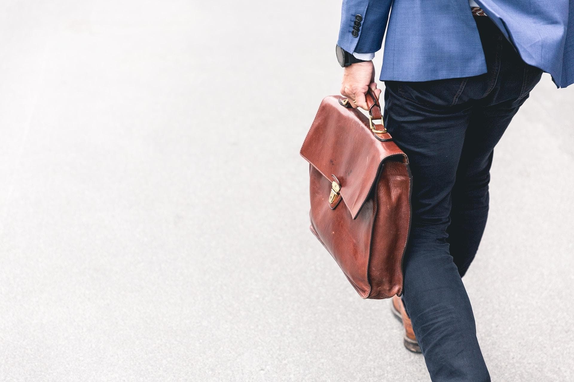 a man in suit walking while holding his work bag